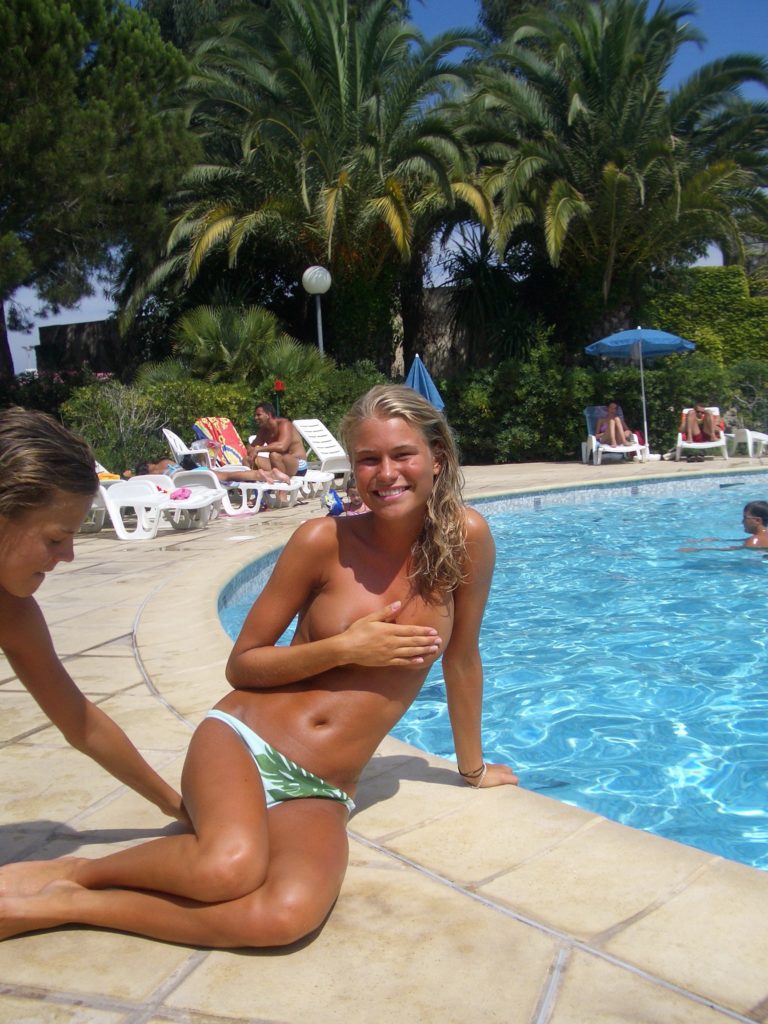 Загорелая блондинка, сидя на краю бассейна, прикрыла свою обнаженную грудь рукой